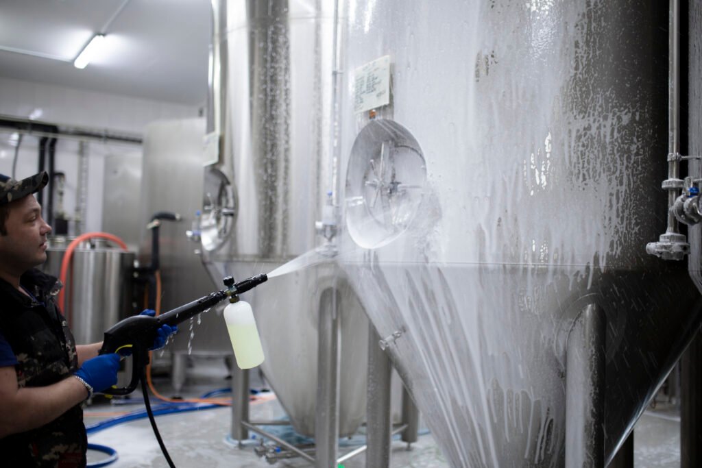 a worker's hand hold a high pressure cleaner gun and put foam on equipment on the factory